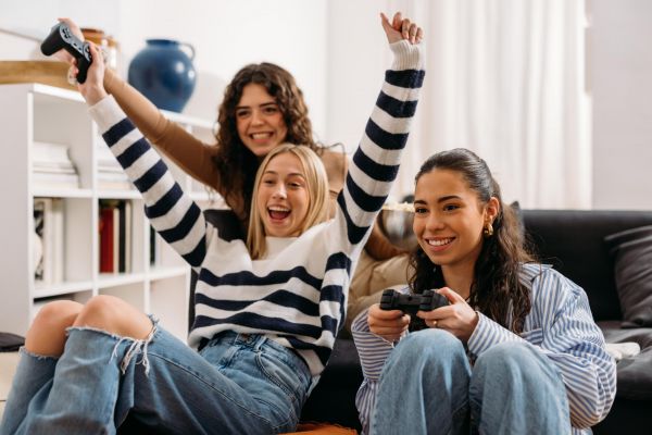 Village Green apartments roommates playing video games on a couch, one cheering. Bookshelf and vase in the background.